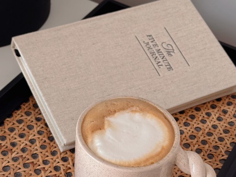 A latte beside a linen planner on a cane tray, calm and intentional morning planning