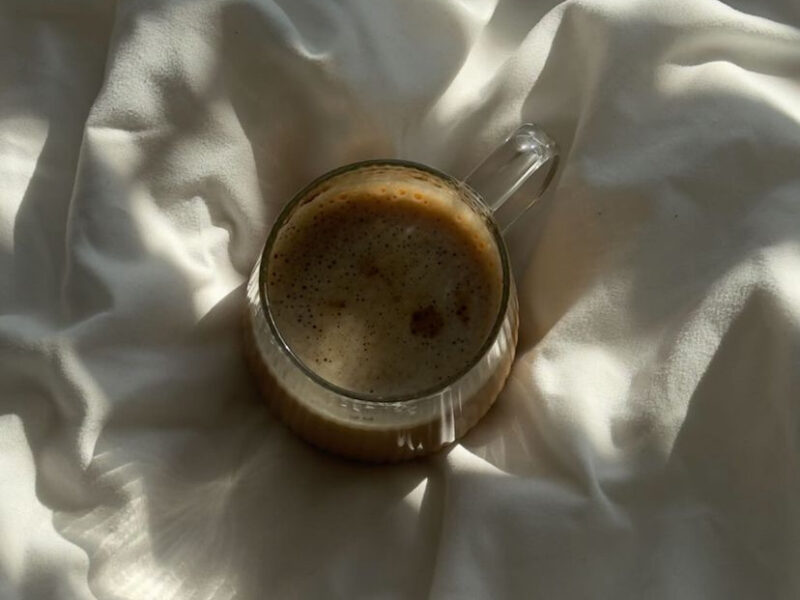 A glass of coffee resting on white linen in soft morning sunlight