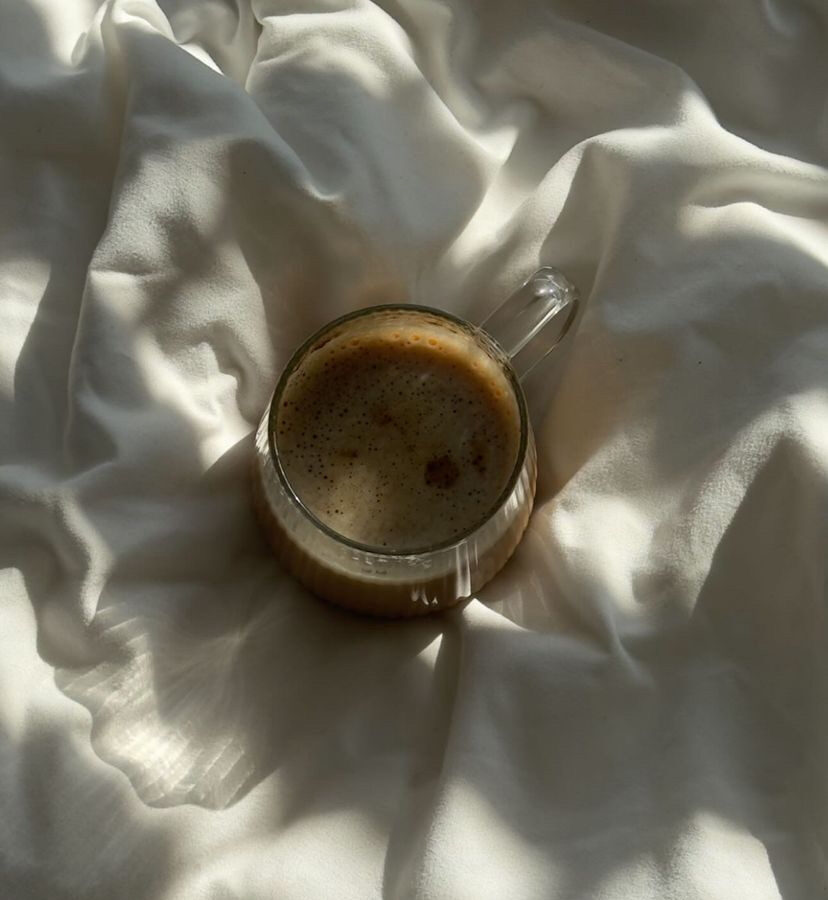 A glass of coffee resting on white linen in soft morning sunlight
